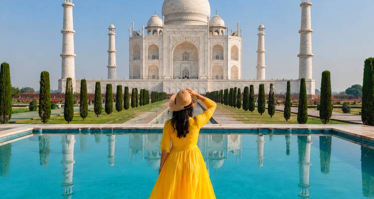 Viajera en un vestido amarillo y sombrero admirando el Taj Mahal desde el otro lado del estanque de agua.