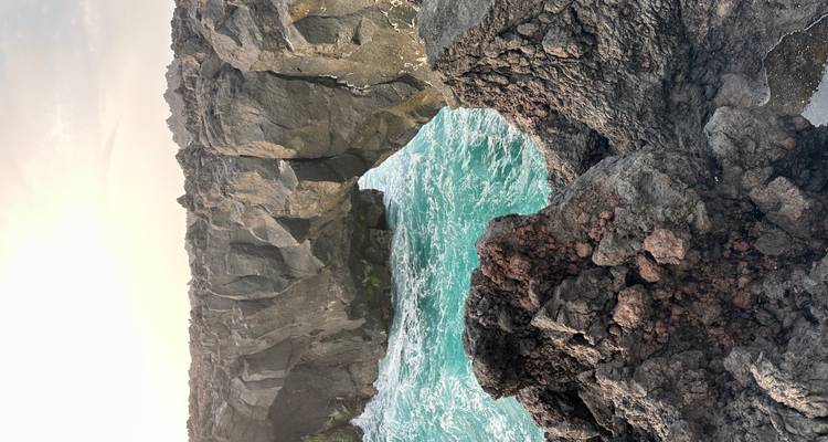Les vagues turquoise illuminées par le soleil déferlent sous une arche de basalte robuste le long d'une côte volcanique à l'heure dorée.