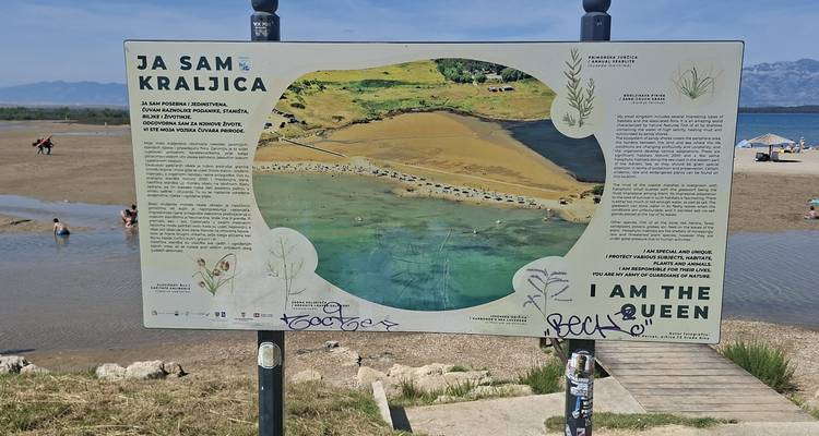 Panneau informatif de carte de plage avec graffiti situé à côté d'un lagon peu profond
