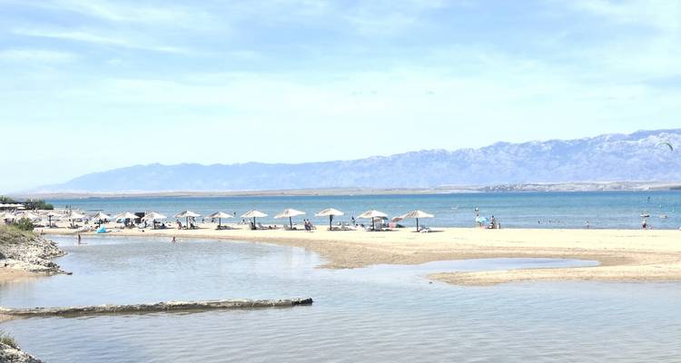Plage ensoleillée croate avec parasols, baigneurs et montagnes lointaines