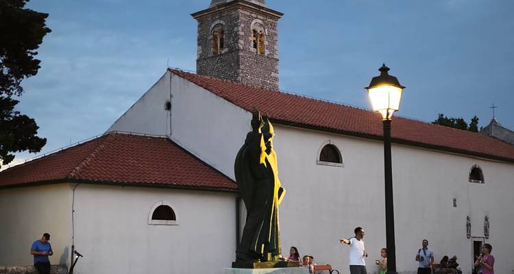Statue et ancienne église en pierre délicatement éclairées au crépuscule avec des visiteurs à proximité