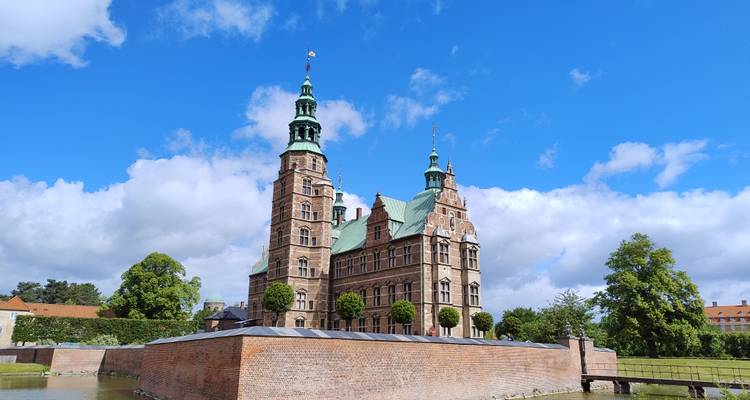Le château de Rosenborg encadré par un ciel bleu, des douves et des remparts en brique avec un feuillage estival éclatant.