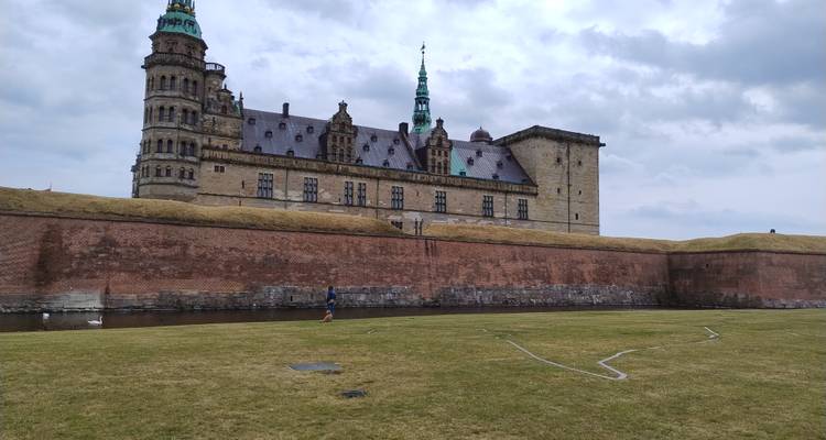 Le château historique de Kronborg s'élevant au-dessus de remparts herbeux et d'une douve sous un ciel menaçant.