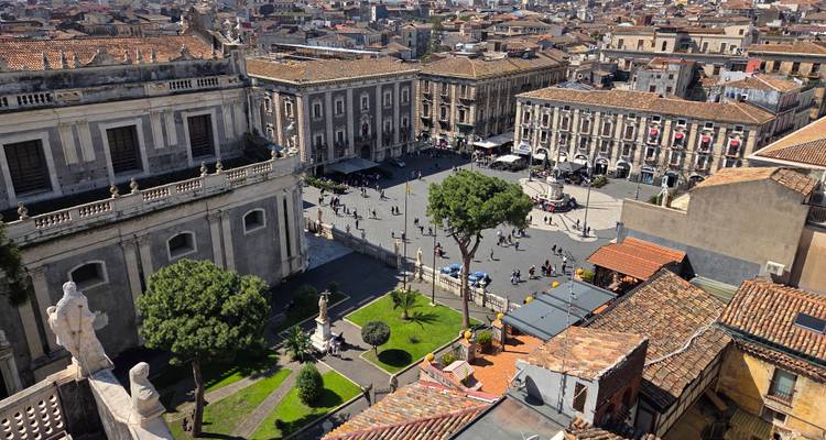 Bird’s-eye view over large historic piazza, baroque buildings and tiled rooftops of city.