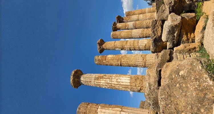 Row of well-preserved sandstone Greek columns rising against a bright blue sky in an ancient temple ruin.