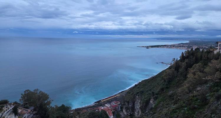 High coastal vantage overlooking turquoise sea and distant shoreline beneath a cloudy sky.