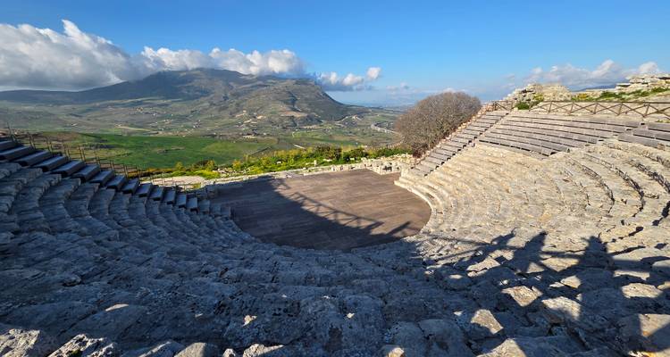 Ancient stone amphitheatre curving toward sweeping rural valley and mountains under clear skies.