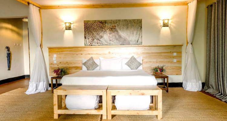 Spacious safari lodge bedroom with wooden furnishings, mosquito-netted bed and wildlife artwork.