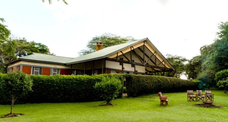 Encantador edificio de alojamiento con paredes de ladrillo y techo verde ubicado detrás de setos bien cuidados y sillas de jardín sobre el césped.