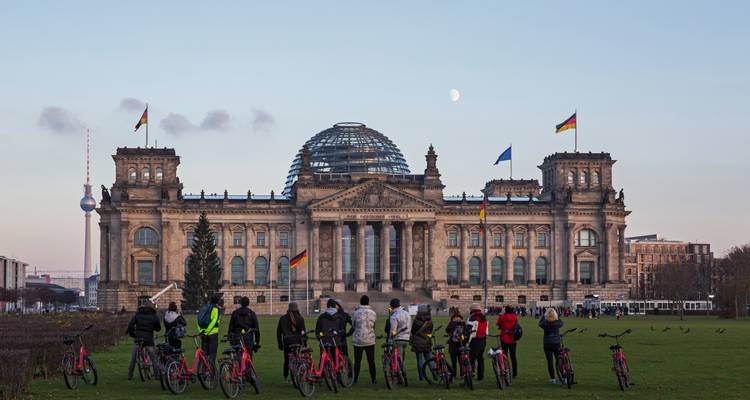 Les cyclistes se rassemblent sur la pelouse devant le bâtiment du Reichstag de Berlin au crépuscule avec la lune au-dessus.