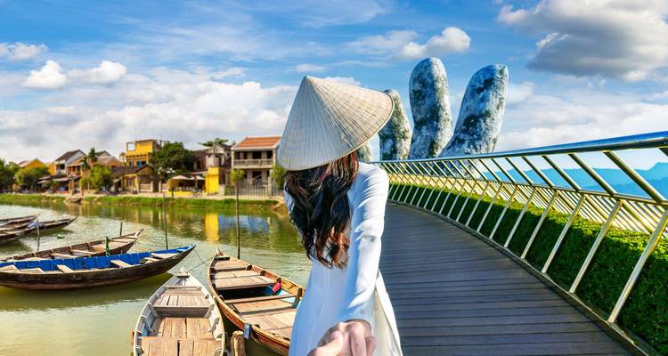Woman in ao dai and conical hat leads the viewer across Da Nang’s Golden Bridge with giant stone hands.