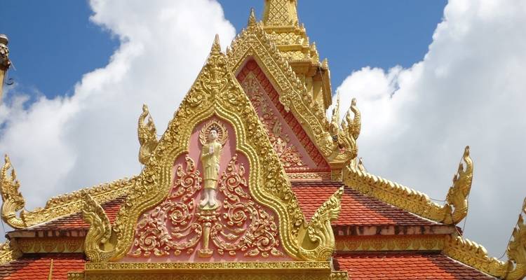 Techo de templo budista dorado y ornamentado con detalles de naga contra un cielo azul brillante.