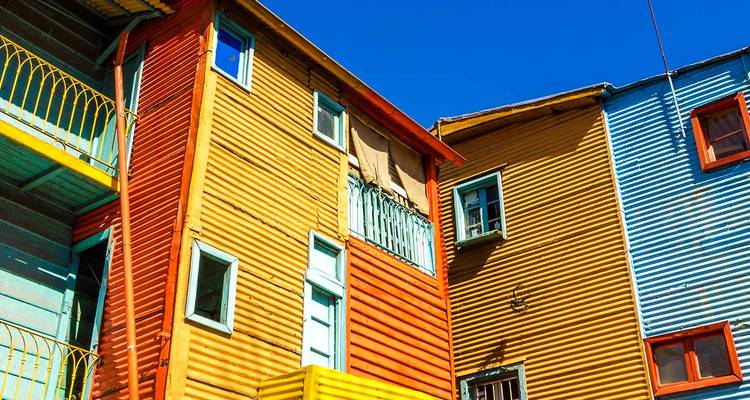 Casas de lámina ondulada de colores brillantes con balcones y ventanas bajo un cielo azul profundo.