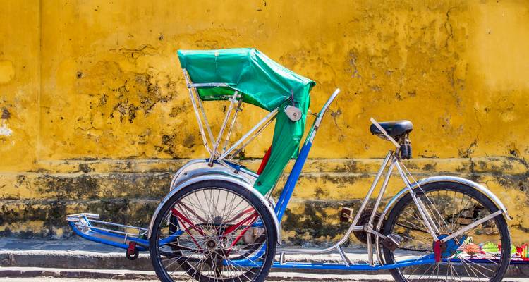 Pousse-pousse cyclo coloré garé contre un mur jaune moutarde usé par le temps
