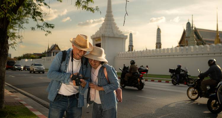 Reifes Ehepaar, das Fotos auf einer Kamera neben den weißen Mauern eines Bangkoker Tempelkomplexes bei Sonnenuntergang überprüft.