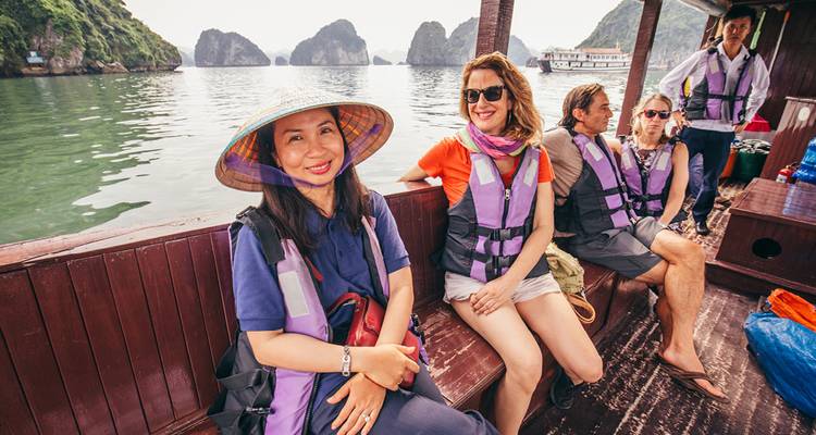 Grupo de turistas con chalecos salvavidas sentados en una barca de madera navegando por la Bahía de Halong.