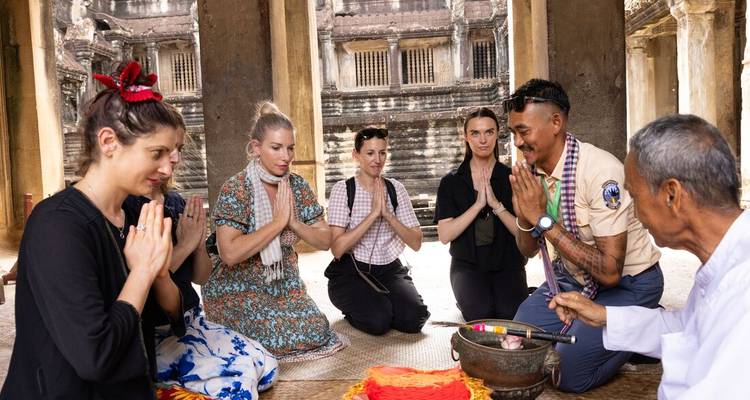 Un grupo de turismo se arrodilla con las manos juntas recibiendo una bendición dentro del templo de Angkor Wat.