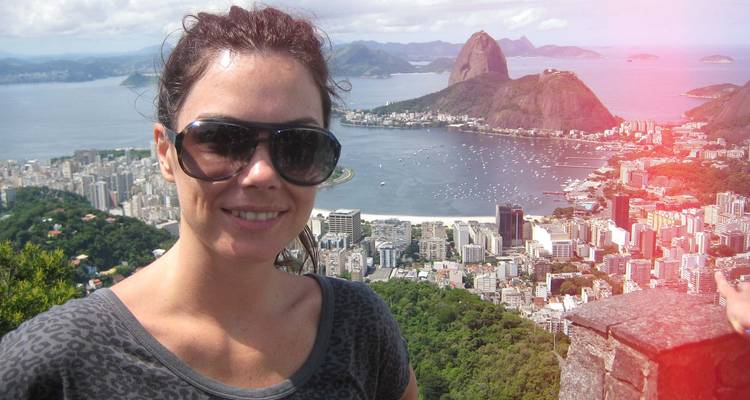 Une femme portant des lunettes de soleil pose à un belvédère surplombant Rio de Janeiro avec le Pic du Pain de Sucre et la côte de la ville en arrière-plan.