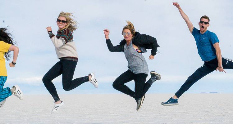 Quatre amis sautent simultanément en l'air sur la vaste étendue blanche du Salar de Uyuni.