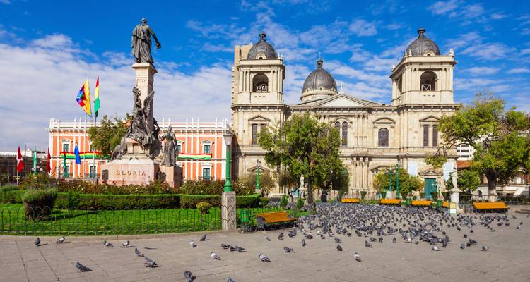 Place remplie de statues devant la Cathédrale de La Paz, avec des pigeons dispersés dans la plaza.