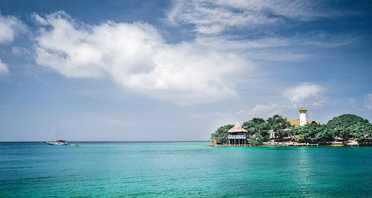 Turquoise Caribbean sea surrounding a lush islet with a thatched roof building and boat