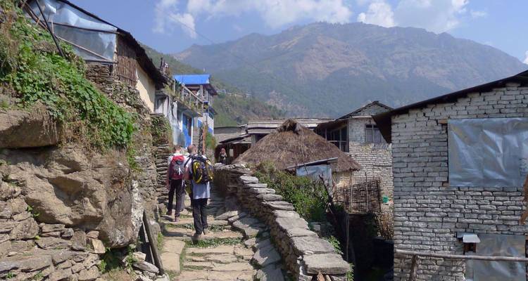 Un groupe de trekking marche dans une ruelle pavée à travers un village de montagne aux toits en terrasse.