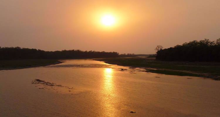 Le soleil doré se couche sur une rivière tranquille serpentant à travers des plaines boisées.