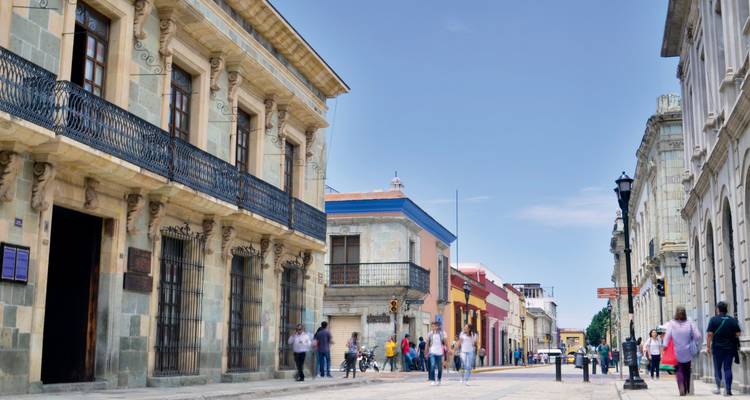 Koloniale Straße in Oaxaca mit Fußgängern und farbenfrohen Fassaden unter einem klaren Himmel.