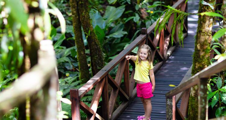 Enfant souriant debout sur une passerelle en bois de jungle entourée d'une végétation verte luxuriante.