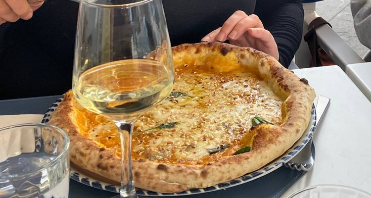 Neapolitan pizza topped with cheese and basil served beside a glass of white wine at a restaurant table