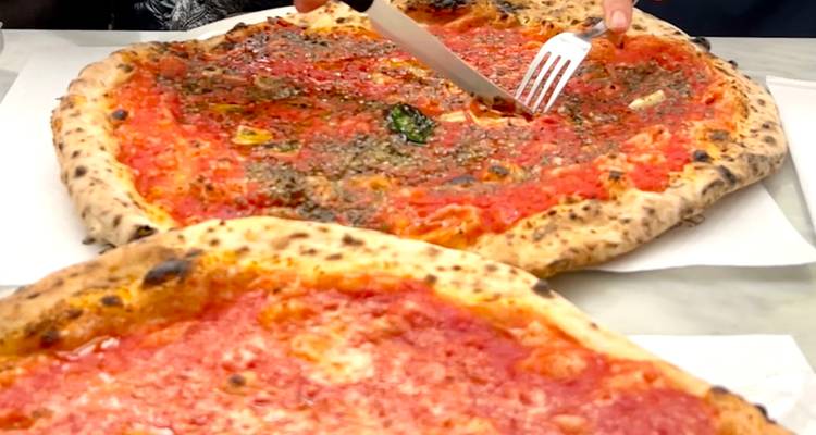 Close-up of two rustic tomato pizzas while a diner cuts a slice with knife and fork
