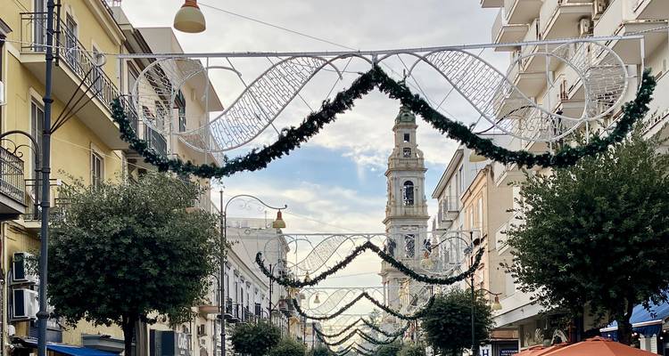 Festively decorated shopping street with garlands and a tall bell tower rising in the background