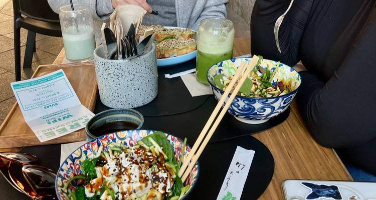 Casual café table with colorful bowls of food, drinks and utensils while diners chat
