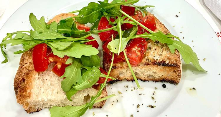 Bruschetta slices topped with fresh tomato pieces and arugula on a white plate