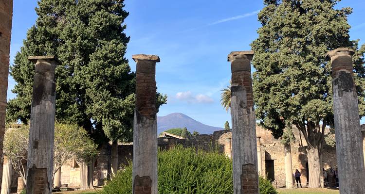 Ancient stone columns framing a distant view of Mount Vesuvius in a sunny archaeological park