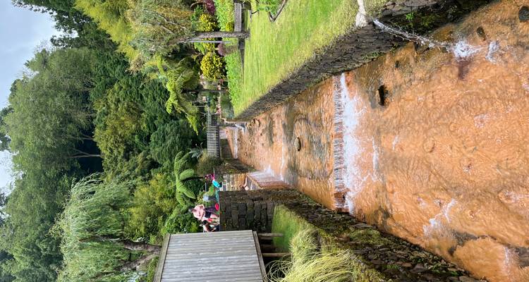 Un cours d'eau thermal de couleur rouille s'écoule à travers des jardins aménagés où les visiteurs se baignent dans de petits bassins.