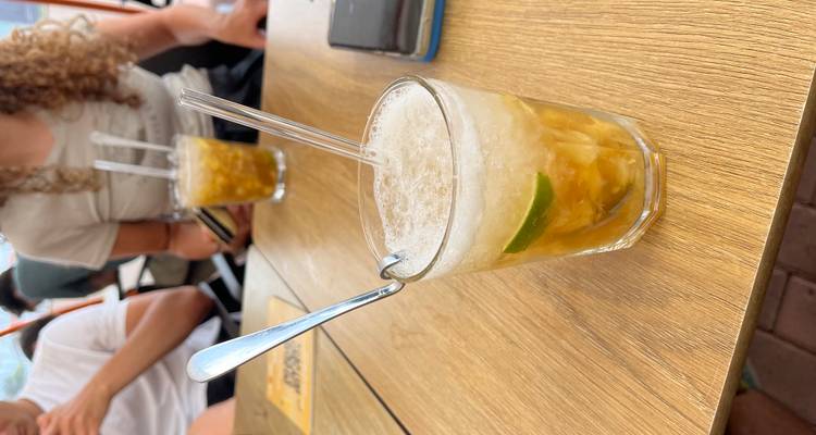 Gros plan d'un cocktail rafraîchissant avec de la glace pilée et du citron vert sur une table de café en bois, les compagnons floués en arrière-plan.