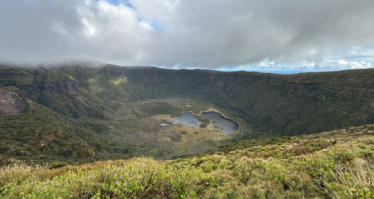 Vue panoramique d'une vaste caldeira volcanique verdoyante contenant plusieurs petits lacs sous un ciel partiellement nuageux.