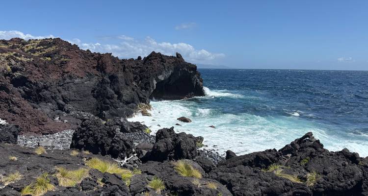 Des falaises de lave noire dentelée rencontrent des vagues turquoise déferlantes sous un ciel bleu clair.