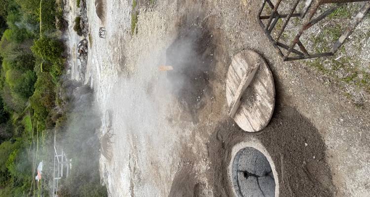 Des fosses de cuisson fumantes avec un couvercle en bois dans un sol volcanique à côté d'une ouverture de source thermale circulaire.