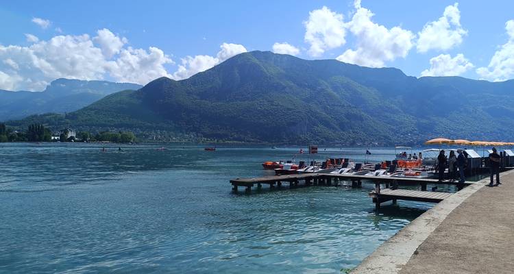 Lac d'un bleu cristallin bordé par des montagnes avec une jetée et des chaises longues sous des parasols brillants