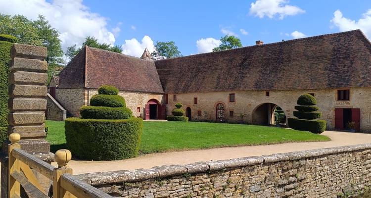 Bâtiments de ferme historiques en pierre avec haies sculptées et pelouse d'un vert éclatant par une journée ensoleillée