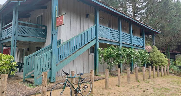Lodge rustique aux rampes en bois teinte bleu-vert, entouré de verdure et d'une bicyclette garée.