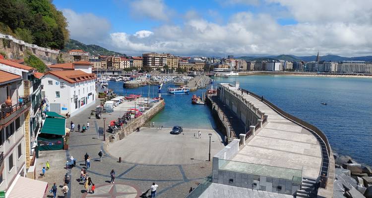 Point de vue élevé surplombant un port de pêche animé, une digue et une plage urbaine qui s'étend sur une grande distance.