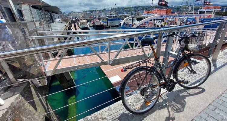 Vélo attaché à la rampe de la marina donnant sur une eau turquoise cristalline et des bateaux amarrés.