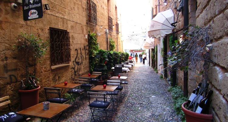 Charmante enge Gasse mit Kopfsteinpflaster, Aussencafé-Tischen und Steinmauern in einer alten italienischen Stadt.