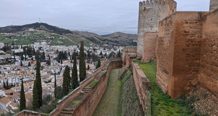 Massive befestigte Mauern der Alhambra mit Blick auf Granada und sanfte Hügel unter bewölktem Himmel.