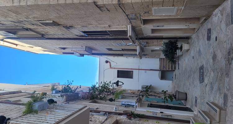 Rustig smal steegje tussen hoge kalkstenen gebouwen onder een helder blauwe lucht.