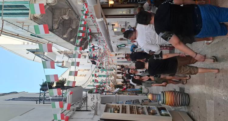 Drukke smalle marktstraat versierd met Italiaanse vlaggen en vol met winkels en mensen.