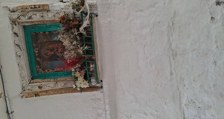 Kleine religieuze kapel omgeven door bloemen in een witgekalkte muur.